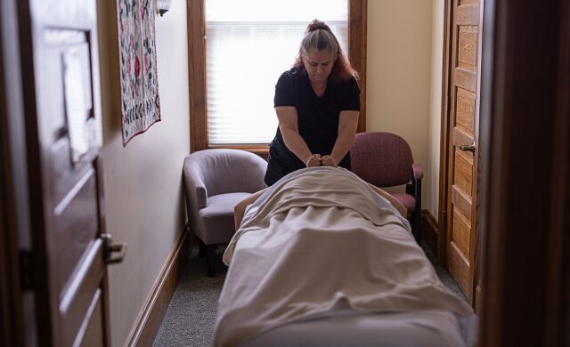 Photo showing massage therapist Diane Long in a session with a client, standing near their head with their hands on the clients upper back.